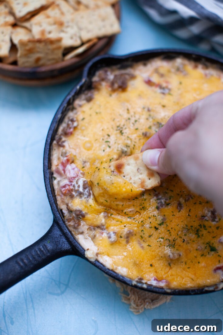 Creamy Skillet Sausage Dip Recipe for Game Day and Parties 3 a hand scooping sausage dip onto a cracker