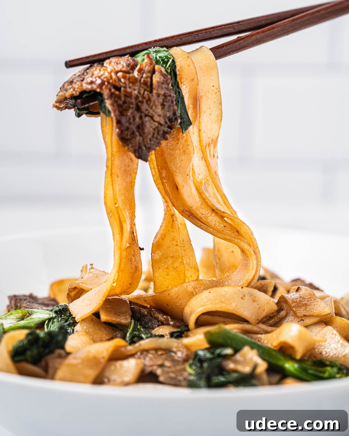 Vietnamese Stir-Fried Hủ Tiếu Noodles with Beef Recipe 11 A pair of chopsticks holding up a bite of noodles, flank steak, and Chinese broccoli.