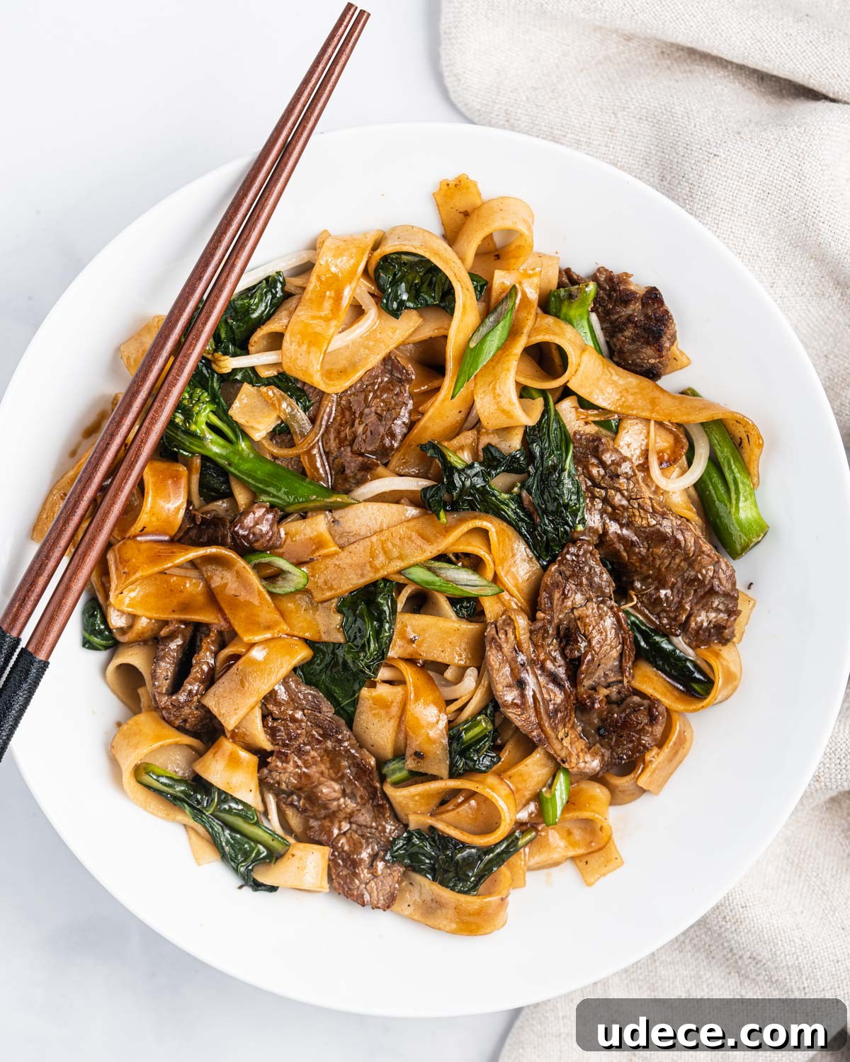 Vietnamese Stir-Fried Hủ Tiếu Noodles with Beef Recipe 10 A white plate with Hu Tieu Xao with beef and vegetables and chopsticks resting on the plate.