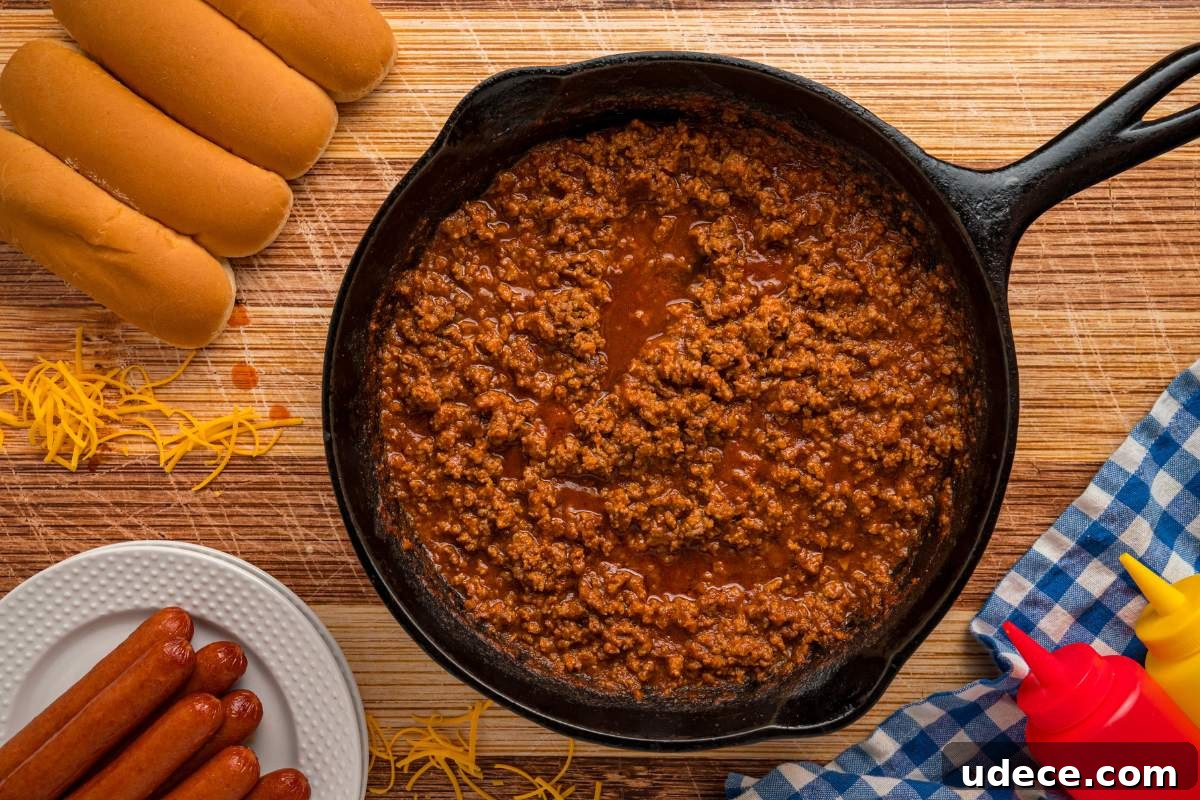 chili in skillet on counter with hot dogs and buns nearby.