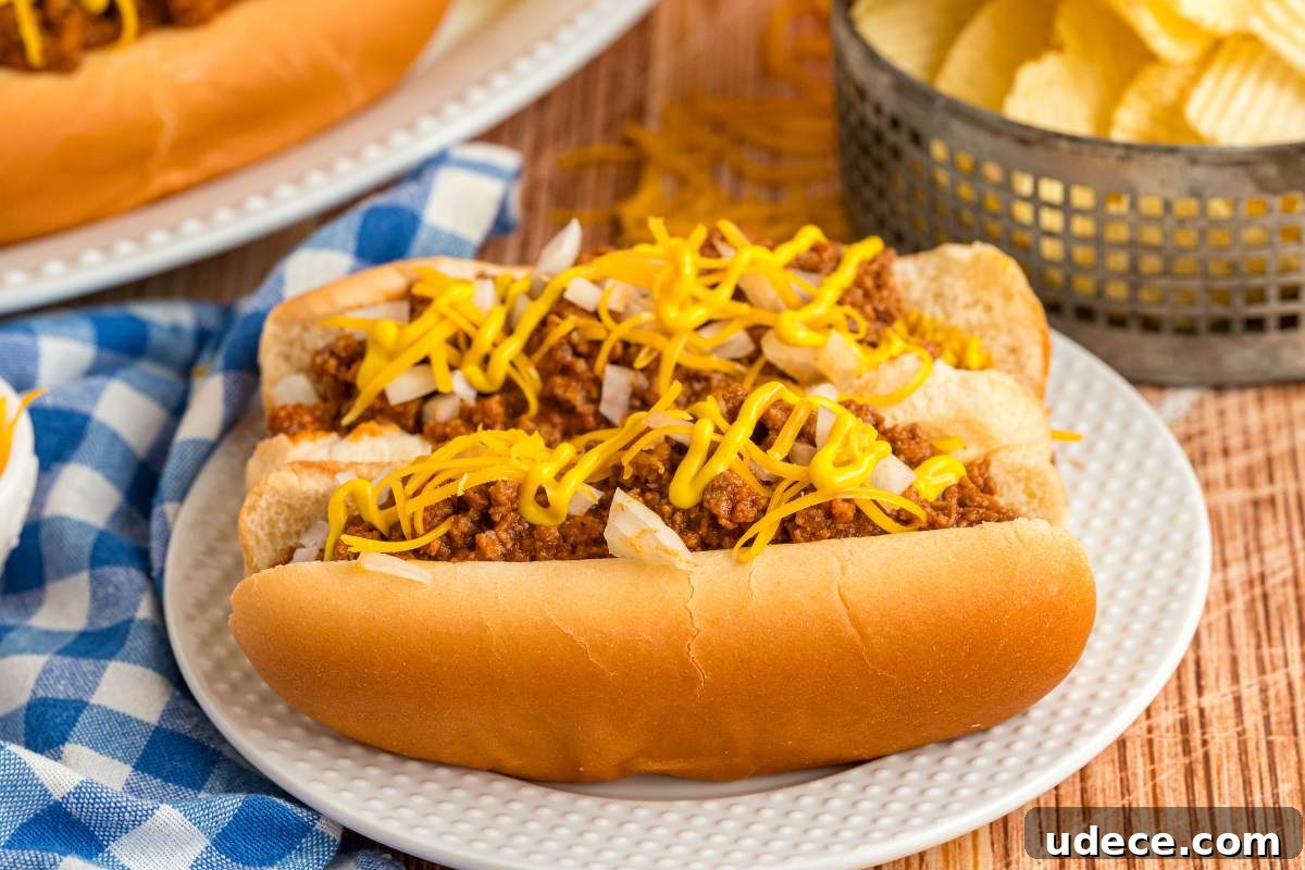 hot dogs topped with chili, mustard, and chopped onions on white plate.