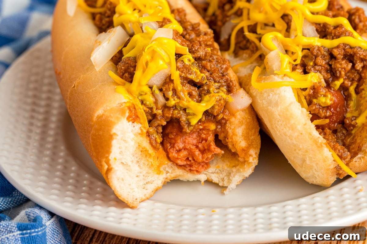 Close-up of a hot dog with a bite taken out, showing chili, mustard, and chopped onions.