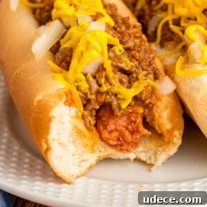 Close-up of a hot dog in a bun with chili, mustard, and chopped onions.