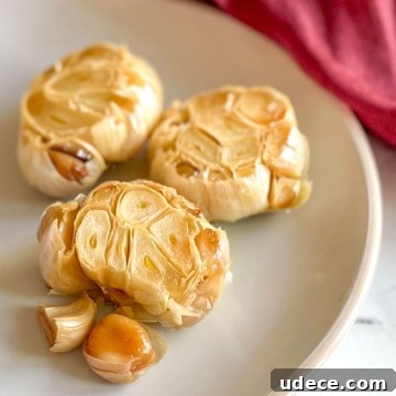 How to Roast Garlic Perfectly for Rich, Sweet Flavor 11 Three heads of roasted garlic sit on a white plate with a red linen in the background.