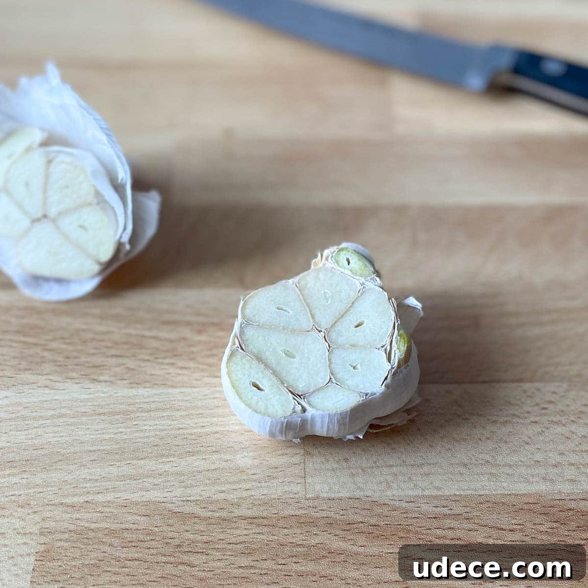 How to Roast Garlic Perfectly for Rich, Sweet Flavor 4 Garlic sliced crosswise to expose the flesh of the cloves on a wooden cutting board.
