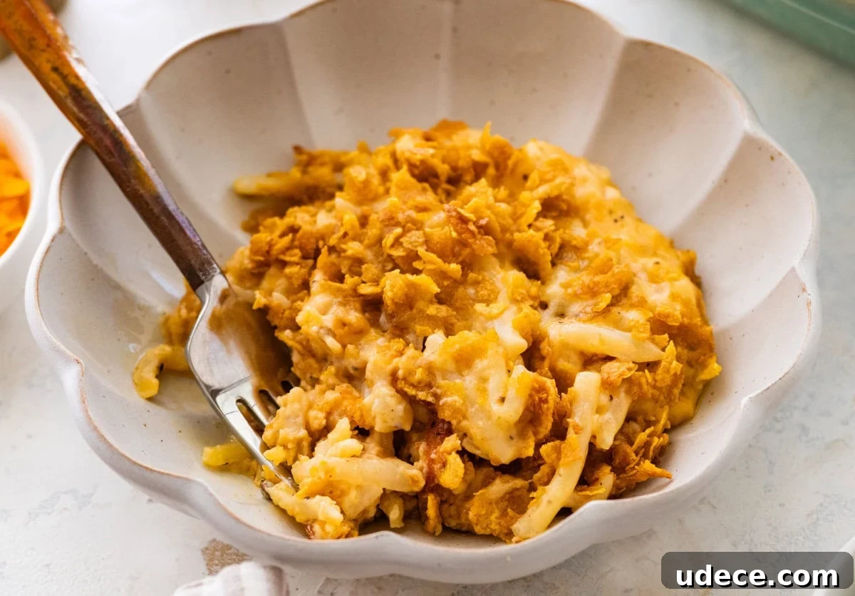 Classic Funeral Potatoes Recipe for Parties and Potlucks 2 A fork holding up one bite of party potatoes with a bowl of more in the back.