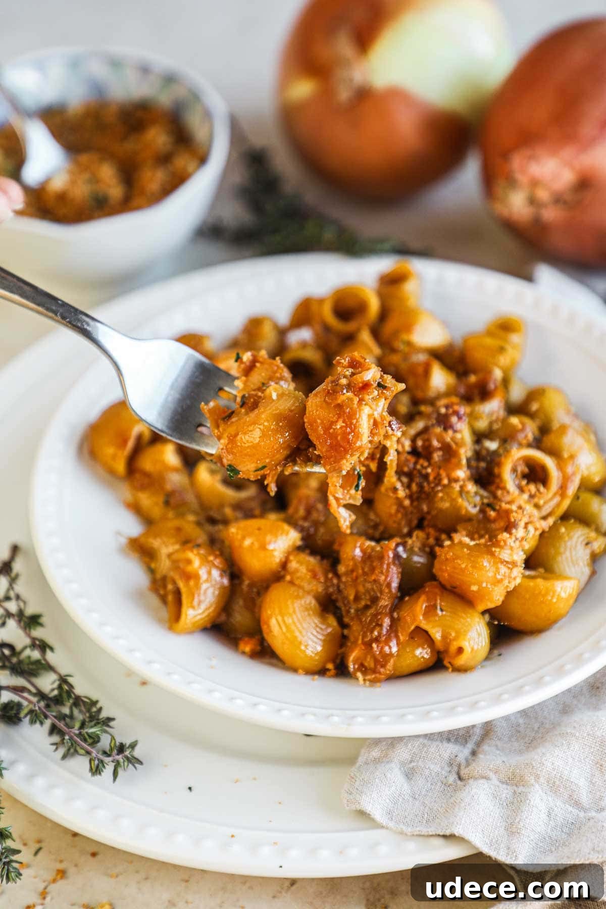Fork holding a bite of caramelized onion pasta topped with herbed toasted breadcrumbs.