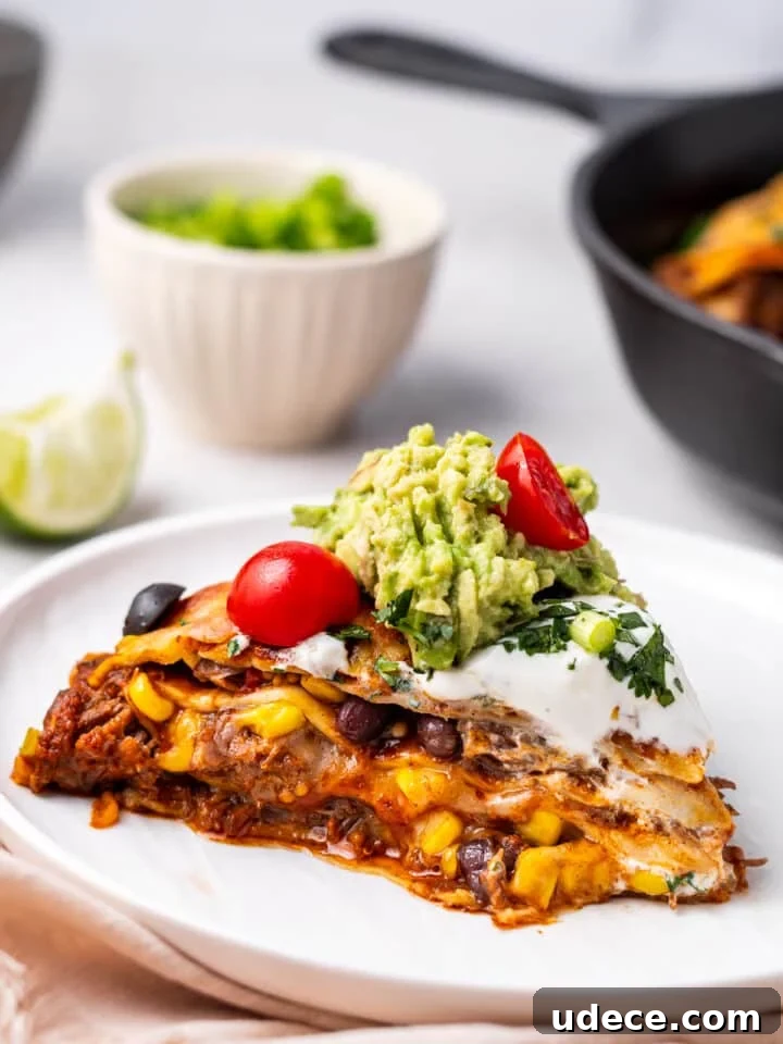 Cheesy Beef Enchilada Pie Recipe for Dinner Crowd-Pleasers 2 slice of beef enchilada pie on a white plate topped with guacamole and tomatoes
