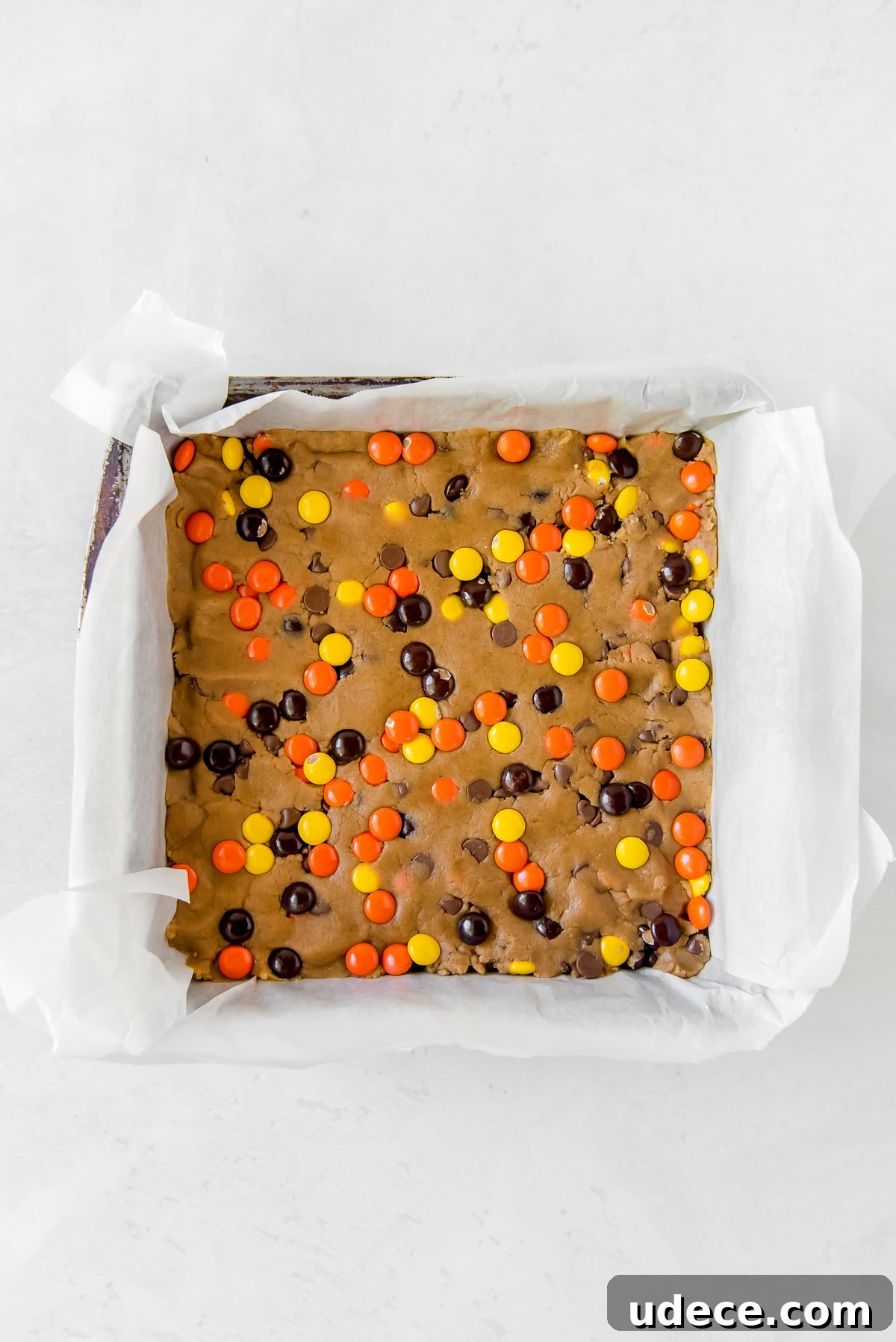 reeses pieces peanut butter blondies dough presses into parchment-lined square baking pan