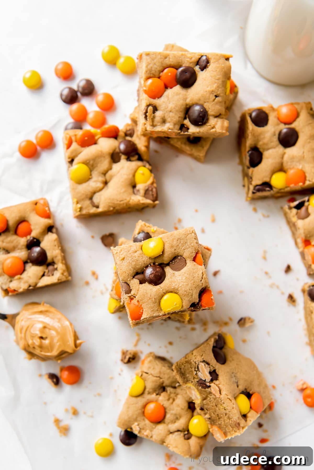 reeses pieces peanut butter blondies on parchment paper next to more reeses pieces candies and spoon of peanut butter