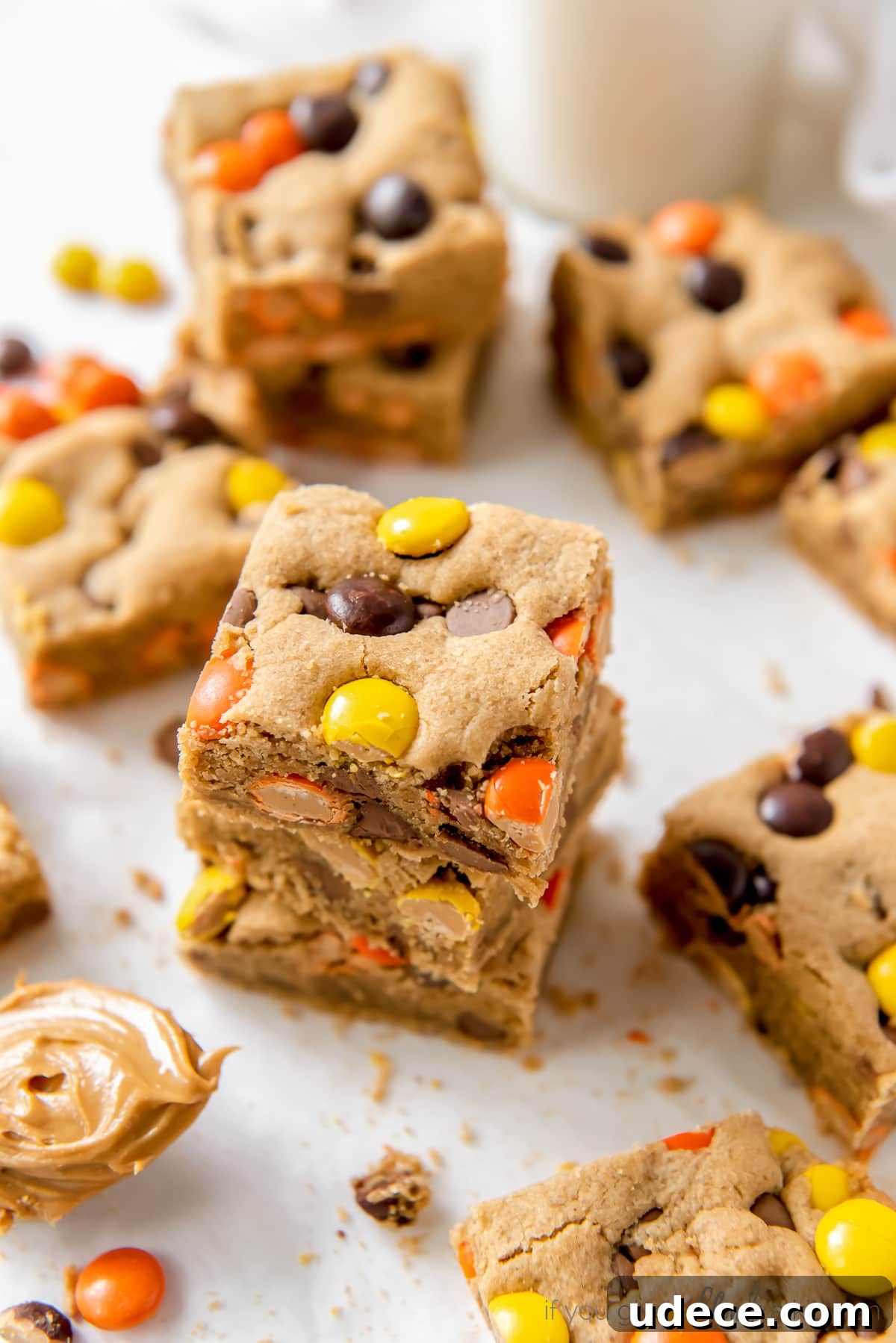 stack of reeses pieces peanut butter blondies on parchment paper next to more blondies