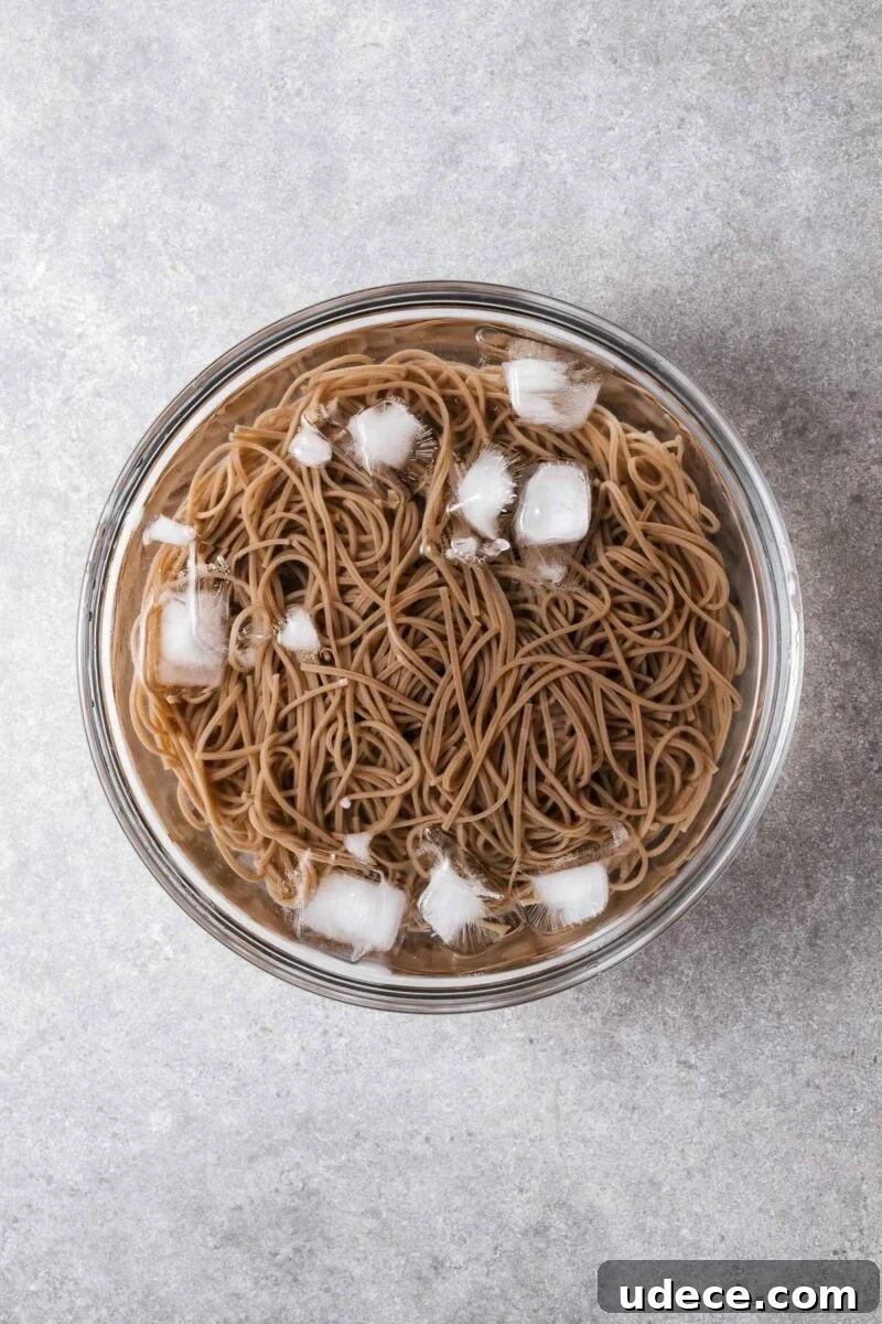 An glass bowl with ice, water and soba noodles.