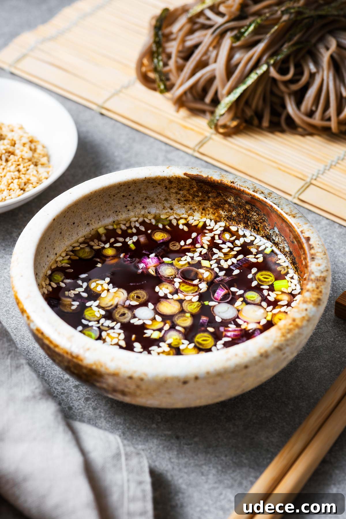 A bowl with Japanese soba noodle dipping sauce sprinkled with sesame seeds and green onions.