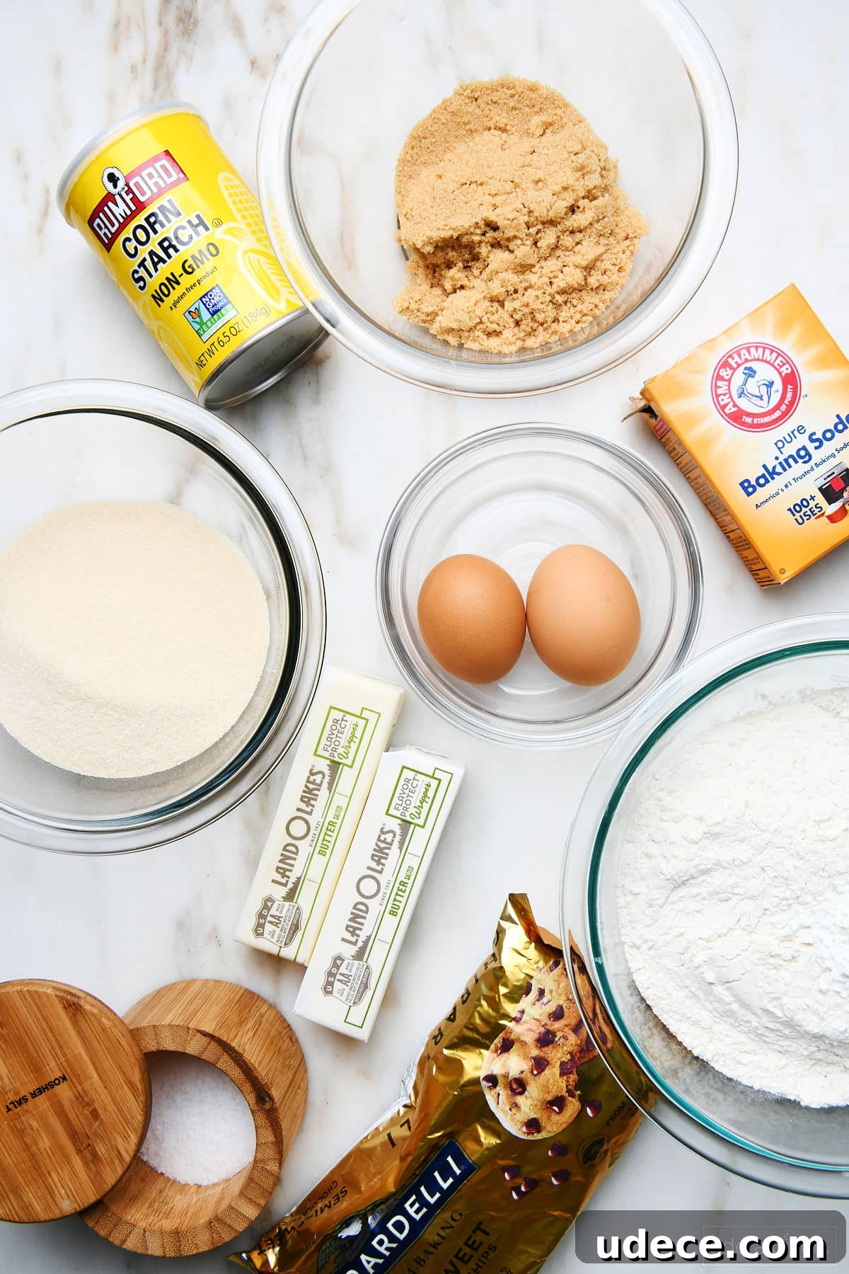 Ingredients for Chocolate chip cookie cake: flour, salt, baking soda, eggs, butter, granulated sugar, brown sugar, and corn starch on a marble countertop.