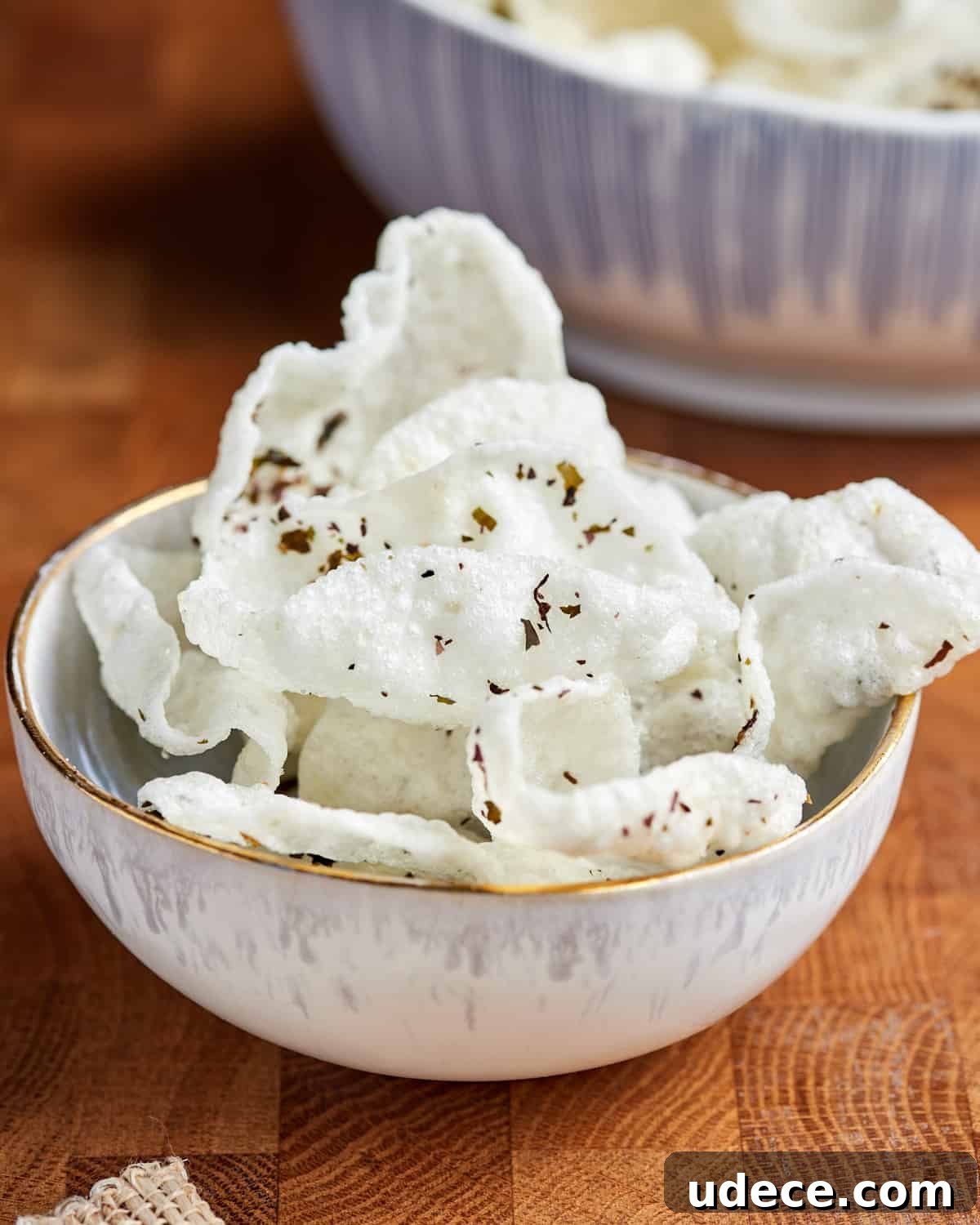Photo showing a bowl full of homemade vegan krupuk set on a Woden table top with a bowl of satay sauce in the background.