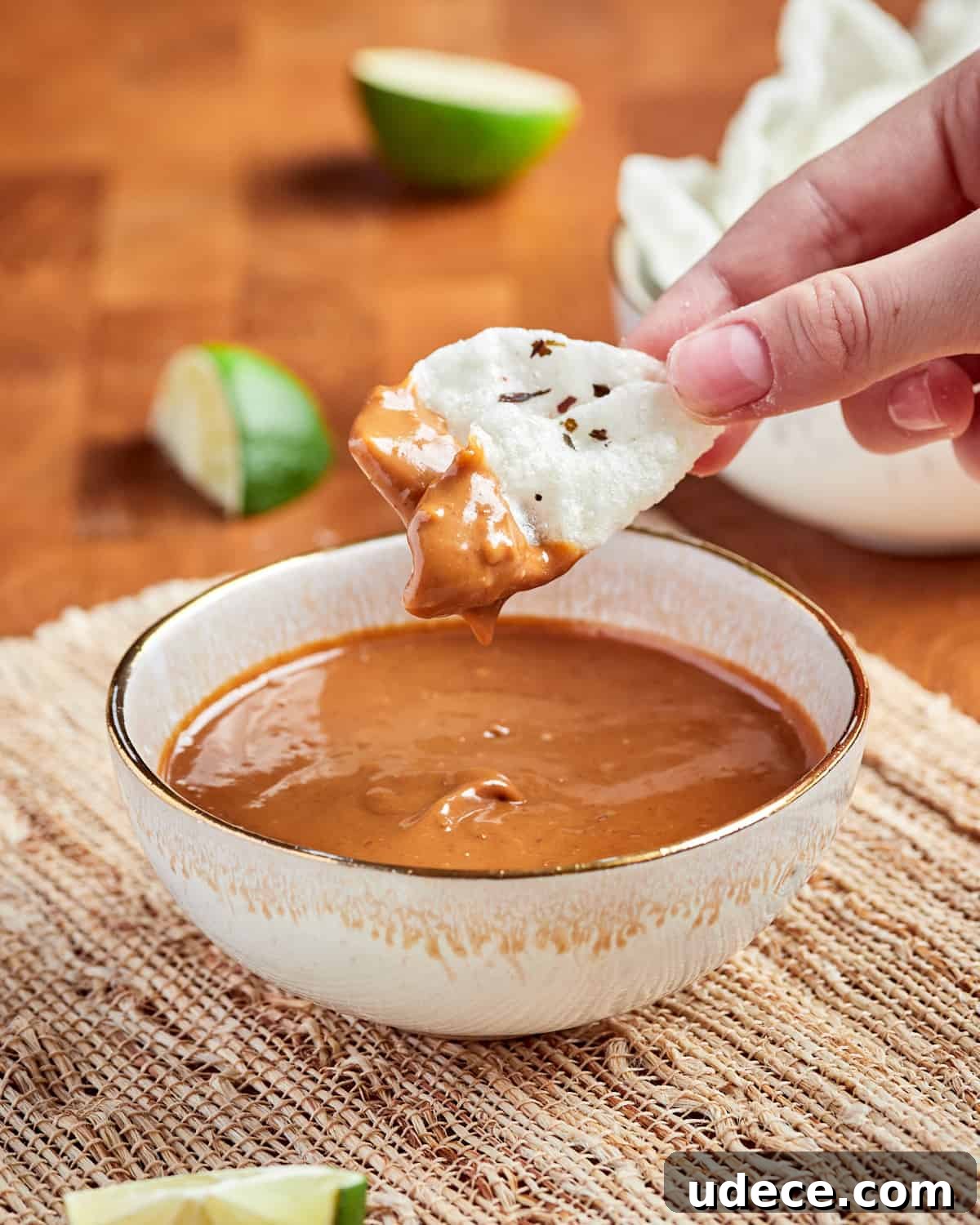 Photo of someone dipping a vegan krupuk cracker into a bowl of Indonesian vegan satay sauce.