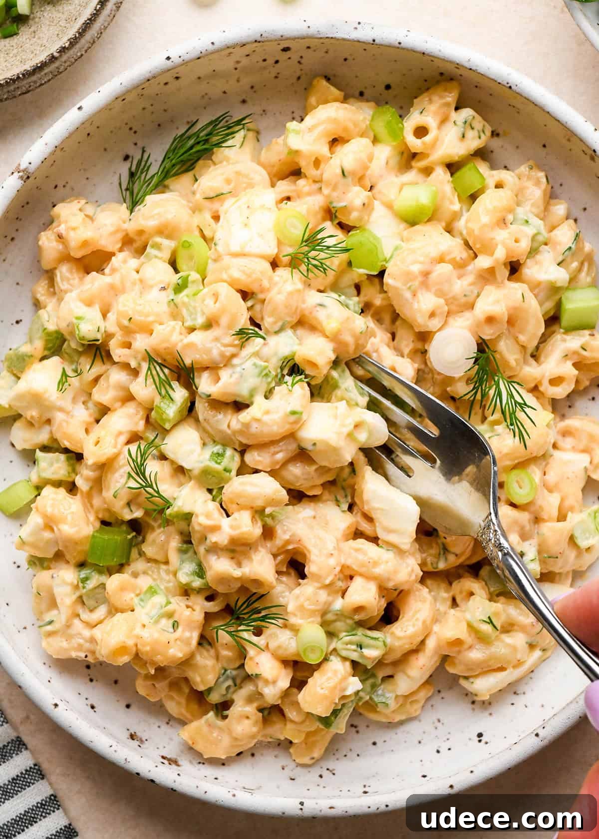 Classic Creamy Macaroni Salad Recipe 10 a fork taking a bite of Macaroni Salad in a bowl