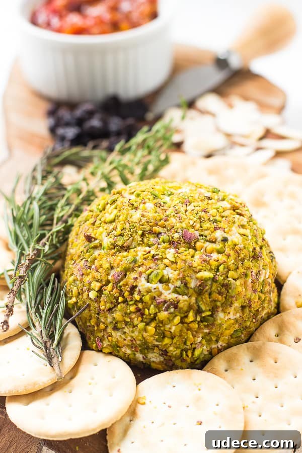 Pistachio-Crusted Vegan Cheese Ball Recipe 5 Pistachio crusted vegan cheese ball on a cheese board with crackers and a sprig of rosemary.