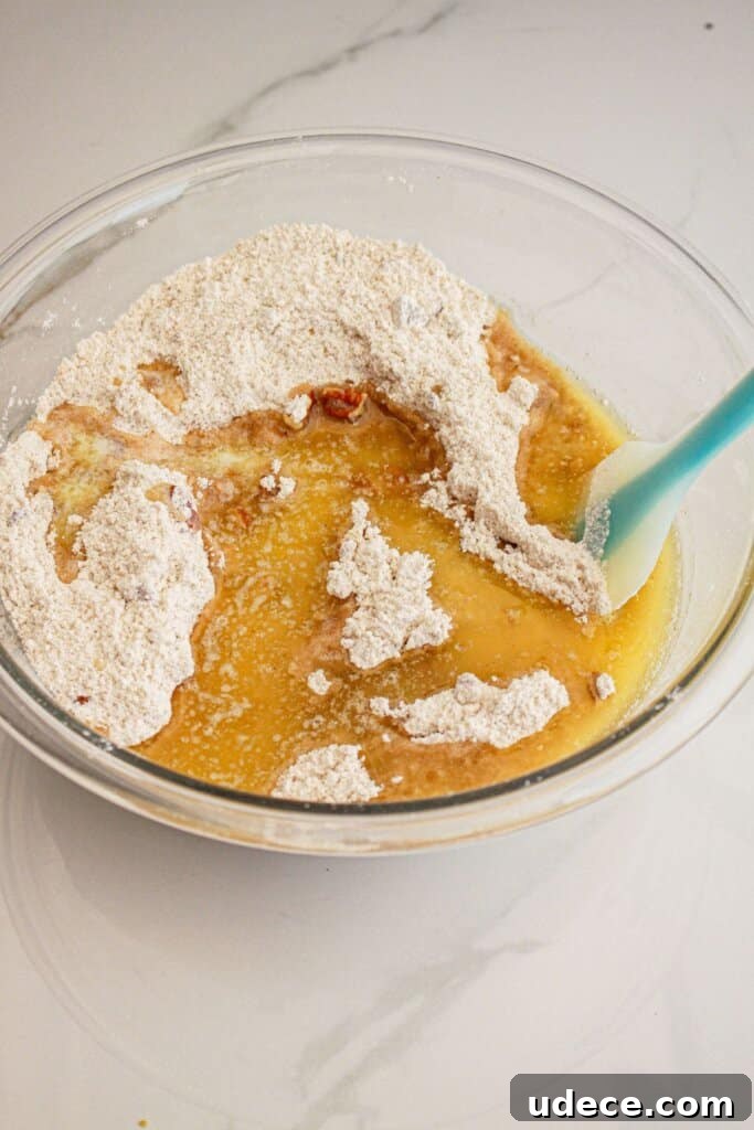 Melted butter being added to flour, brown sugar mixture in a large glass bowl.