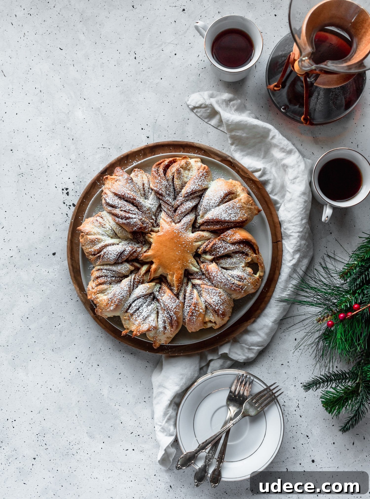 Cookie butter cinnamon star bread on a grey counter next to white plates, coffee, and garland