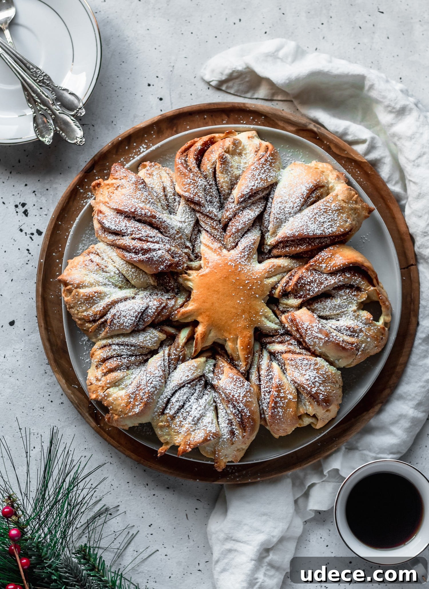 Christmas bread on a white linen next to plates and garland with a white background