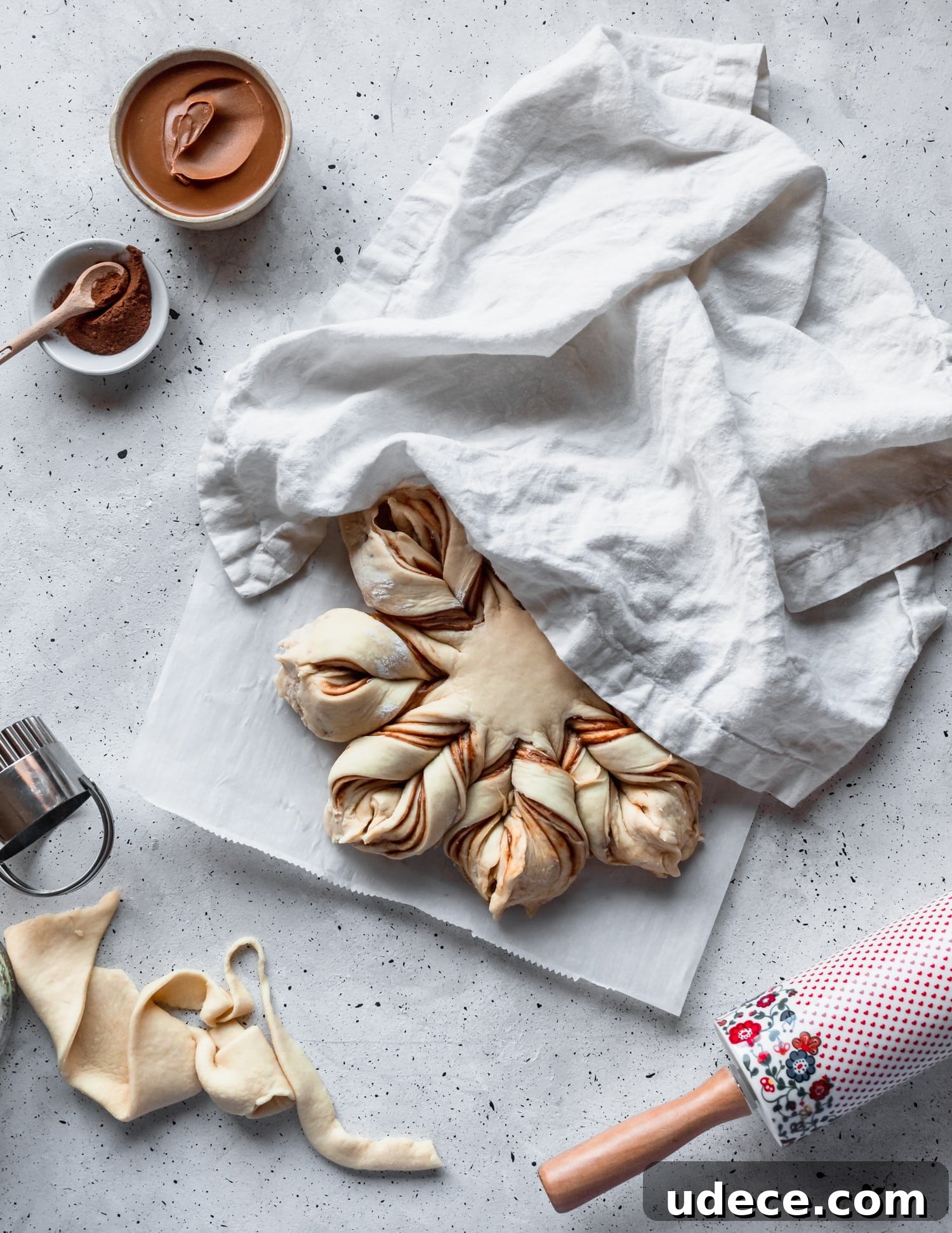 Cookie butter cinnamon star bread rising under a white linen next to a rolling pin