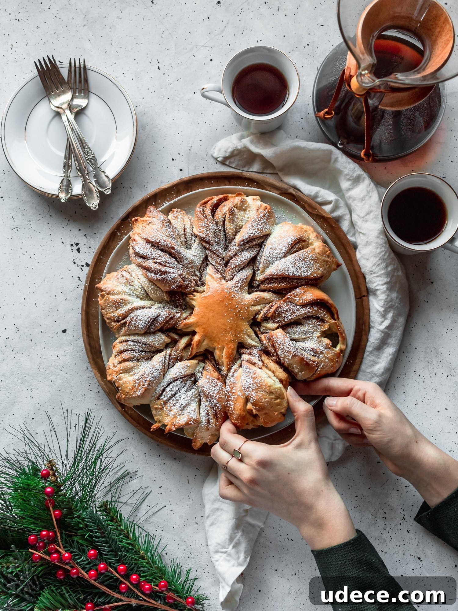A woman pulling a piece of cookie butter cinnamon star bread on a white table next to coffee and garland