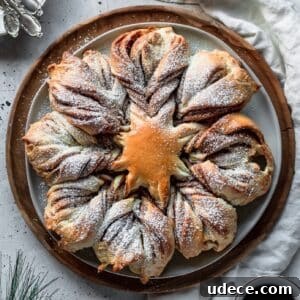An overhead image of cinnamon star bread on a wood tray placed on a grey table next to a white linen