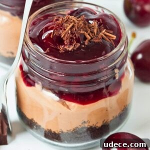 close-up of no bake chocolate cherry cheesecake in a mason jar with layers of oreo crust, chocolate filling and cherries.