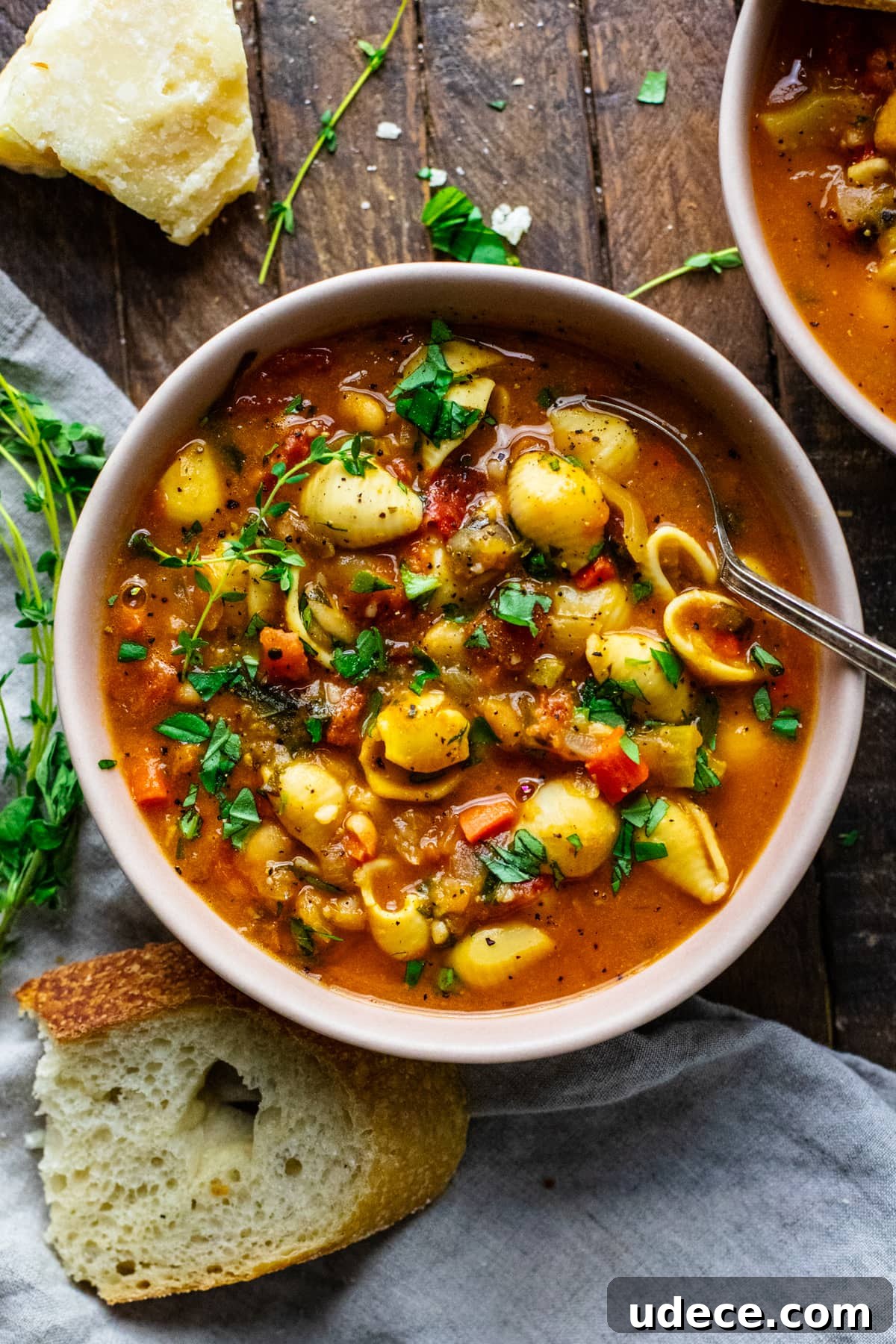 a bowl full of pasta fagioli soup on a wooden background with bread slices next to it.