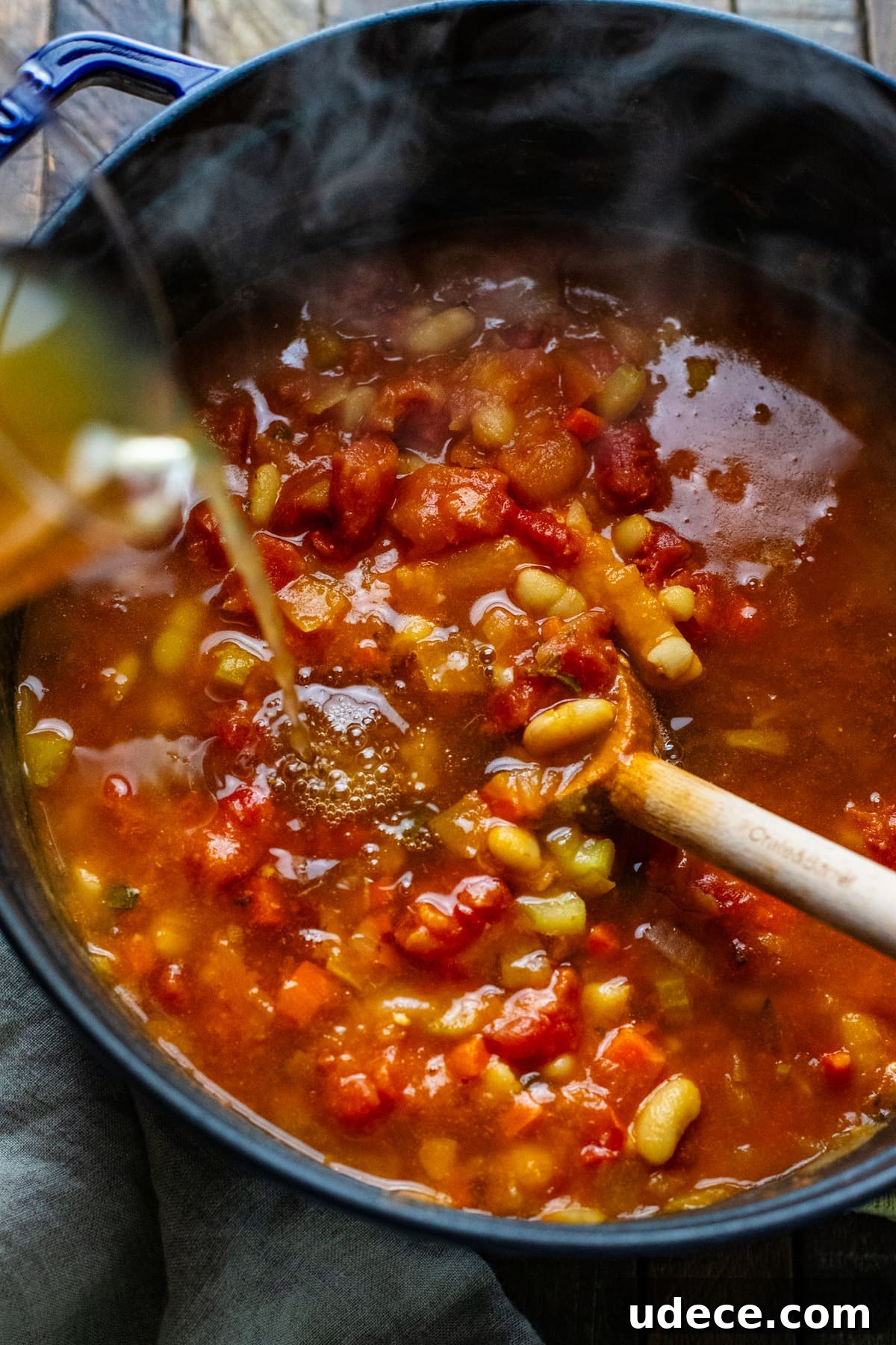 broth being poured into soup with tomatoes in it.