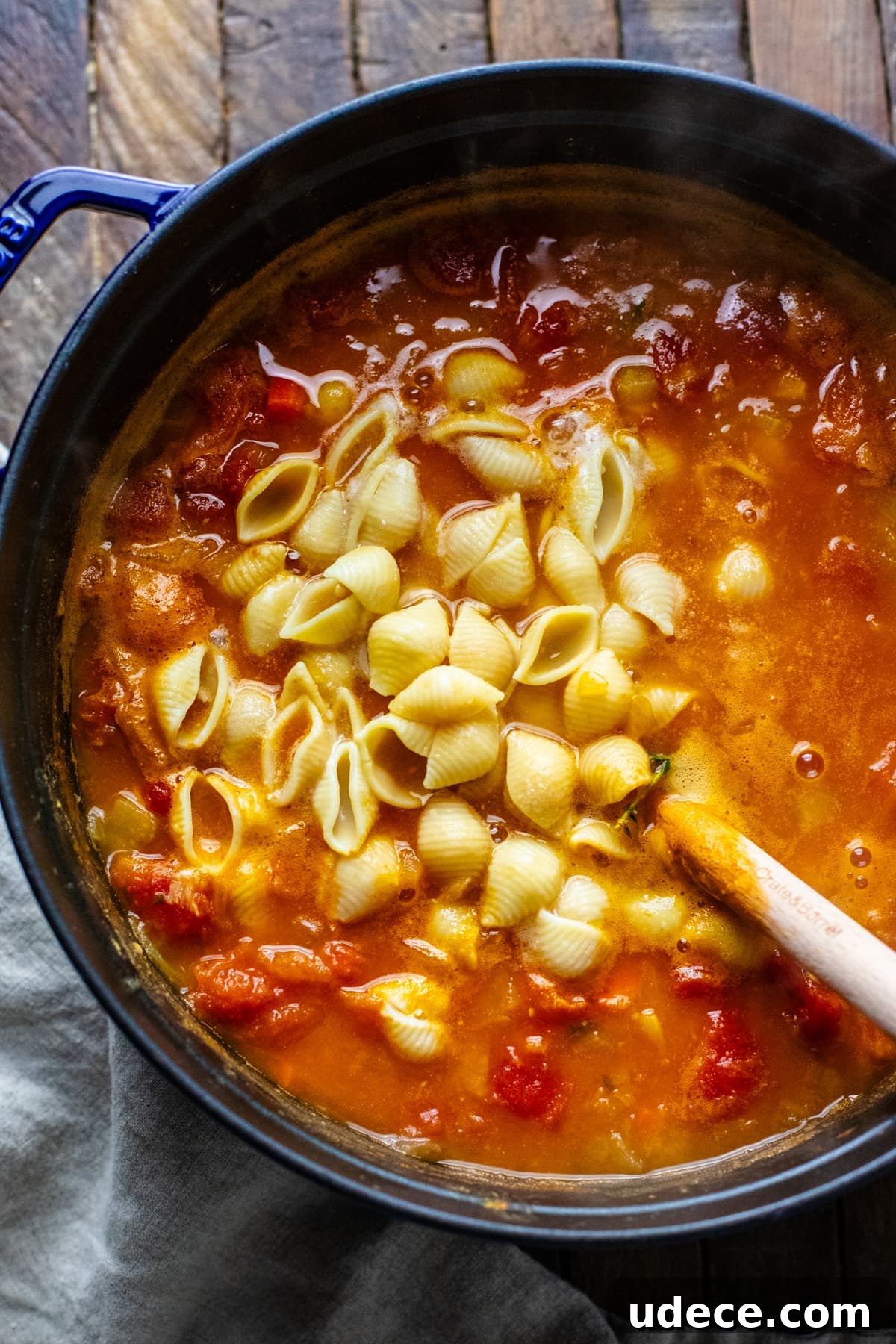 a black pot with red soup in it with pasta shells being mixed in.
