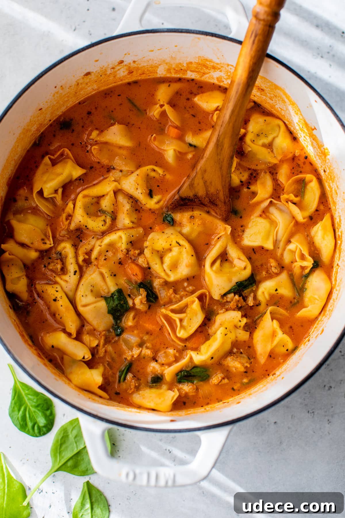sausage tortellini soup in a dutch oven with a wooden soup