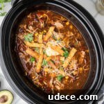 An overhead shot of a black crock pot with some chicken tortilla soup ready to be eaten.