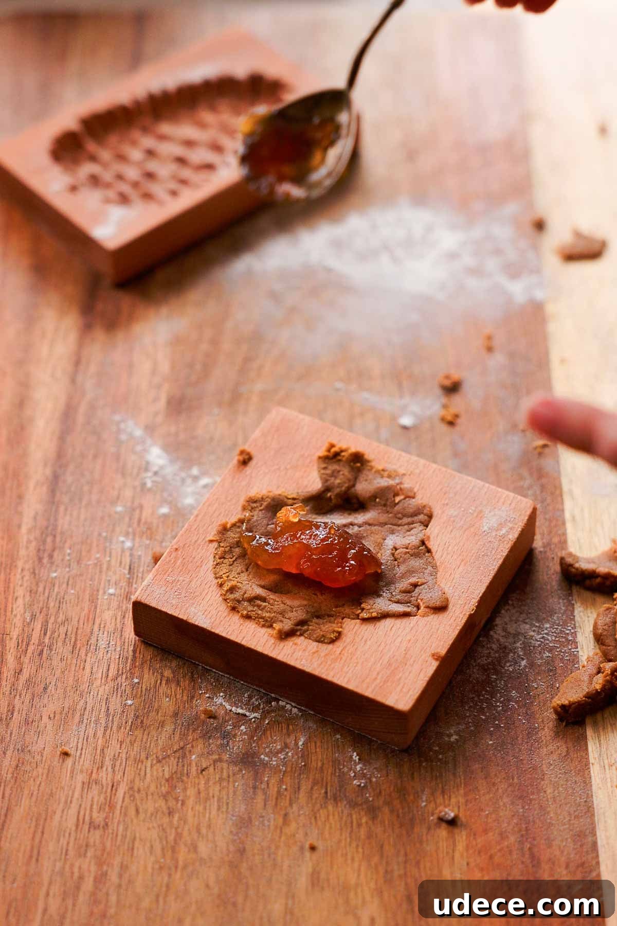 adding a teaspoonful of jam into the center of gingerbread cookie dough inside a wooden cookie mold