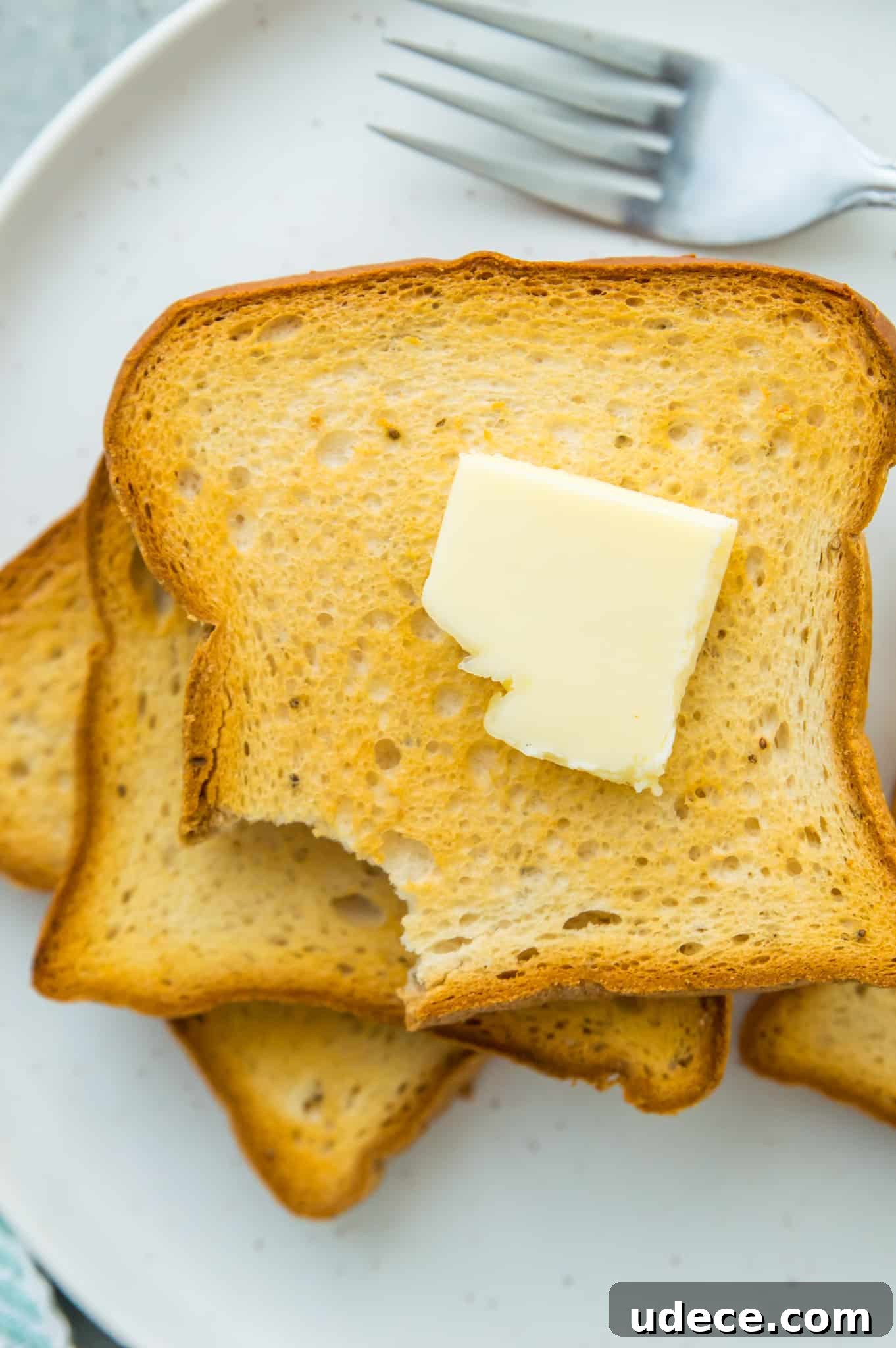A stack of toast on a plate with butter on top.