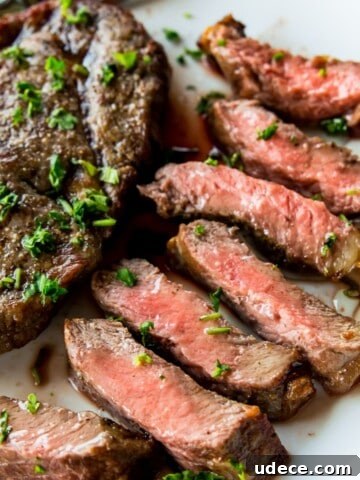 A piece of cut up steak on a plate with a full piece of steak beside it.
