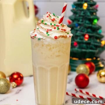 Tall glass of eggnog dirty soda topped with whipped cream, red and green holiday sprinkles, and a dusting of cinnamon, served with a red-striped straw.