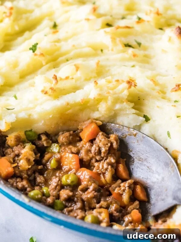 Close-up view of a spoon scooping out meat and veggies from a dish of shepherd's pie.