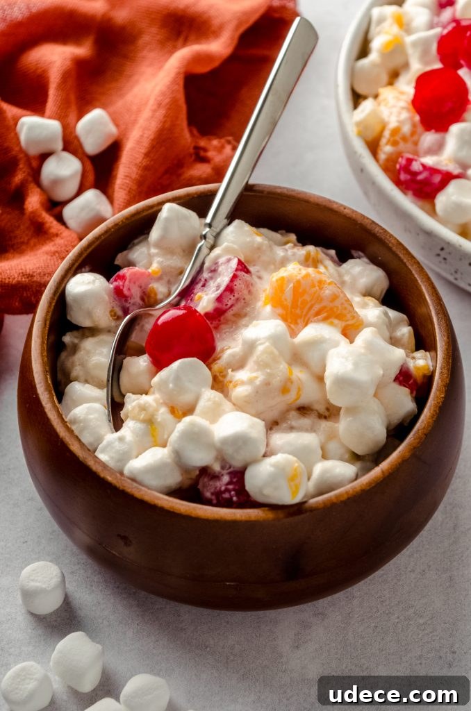 A small brown wooden bowl filled with ambrosia salad and a spoon.