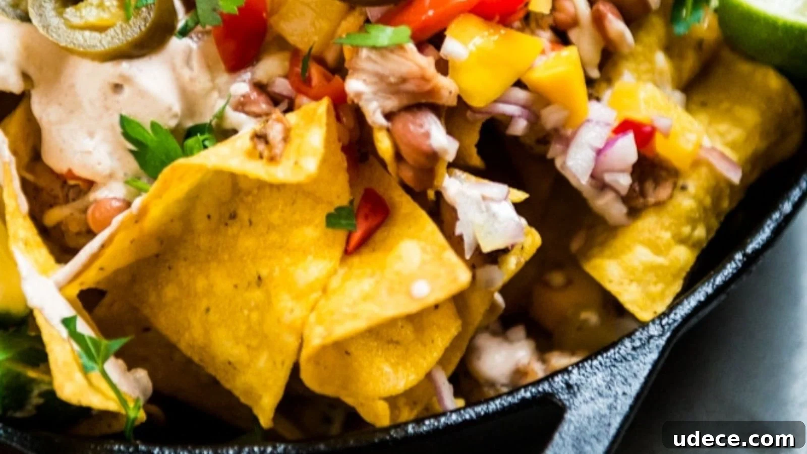Close-up of loaded nachos topped with chopped onions, bell peppers, jalapeños, beans, and a creamy sauce in a black bowl.