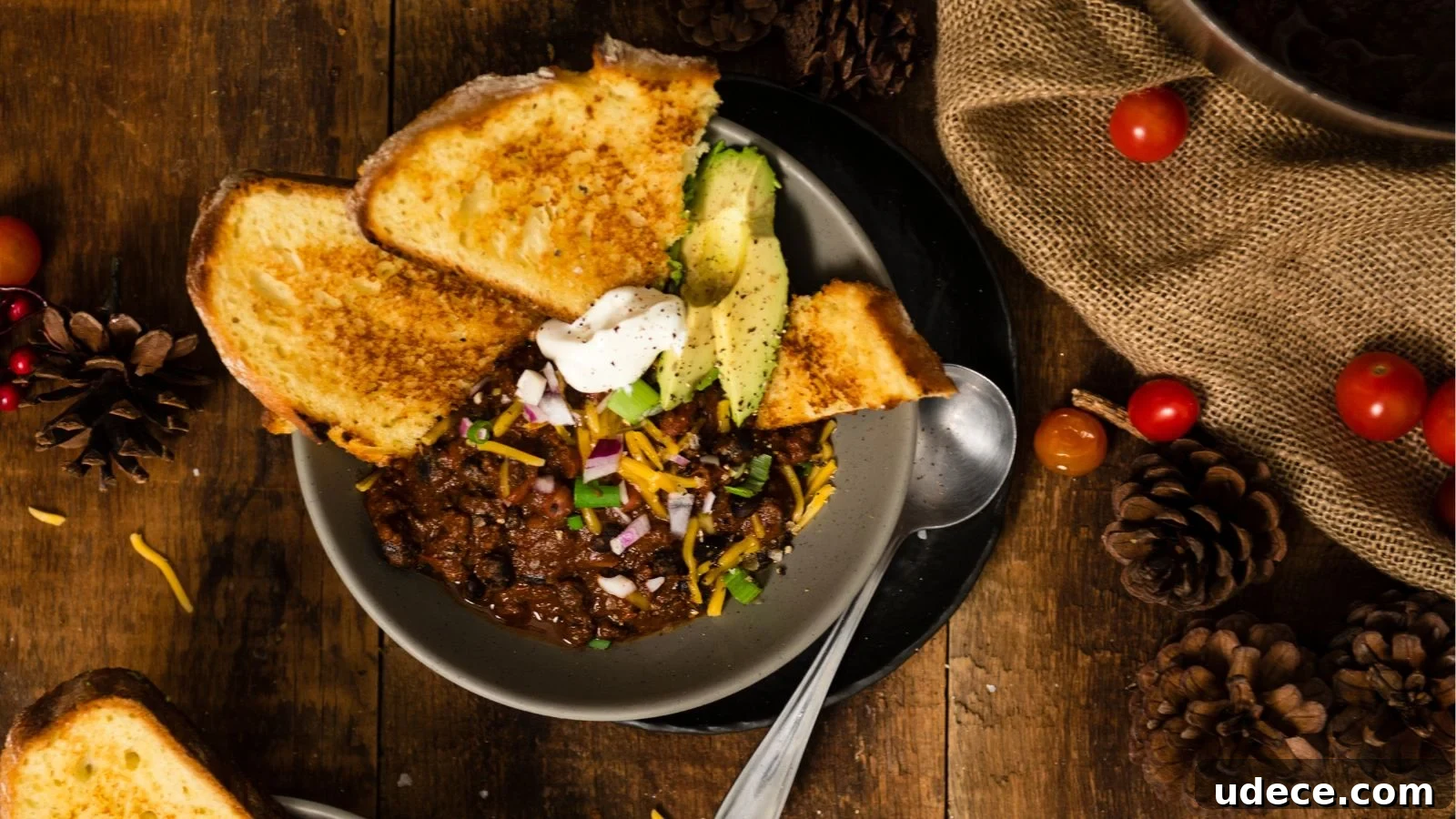 A bowl of chili topped with cheese, red onions, avocado, and sour cream, served with toasted bread.