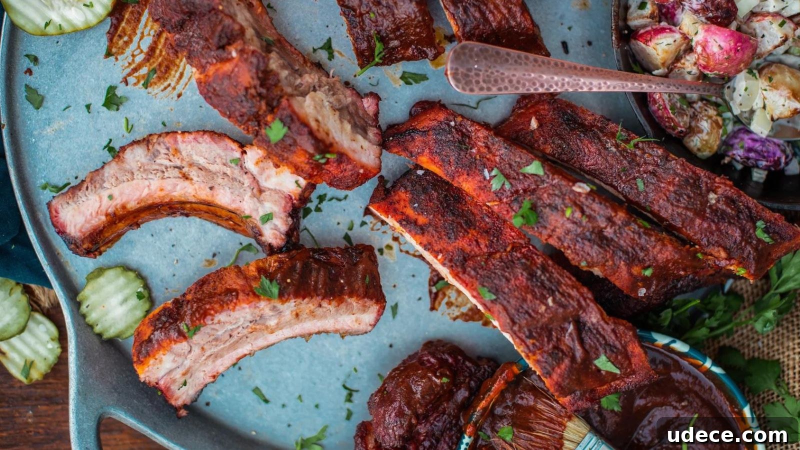 Plate of grilled ribs with parsley garnish, served with pickles and potato salad.