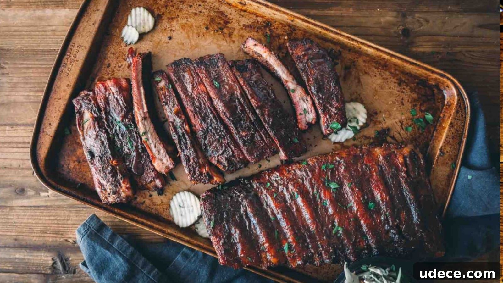 A tray of barbecued ribs with visible grill marks, garnished with herbs. Wavy potato chips are placed next to the ribs.