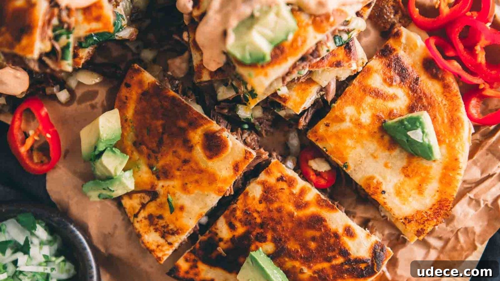 Close-up of grilled quesadillas with avocado chunks and sliced red chili peppers on top, arranged on parchment paper.
