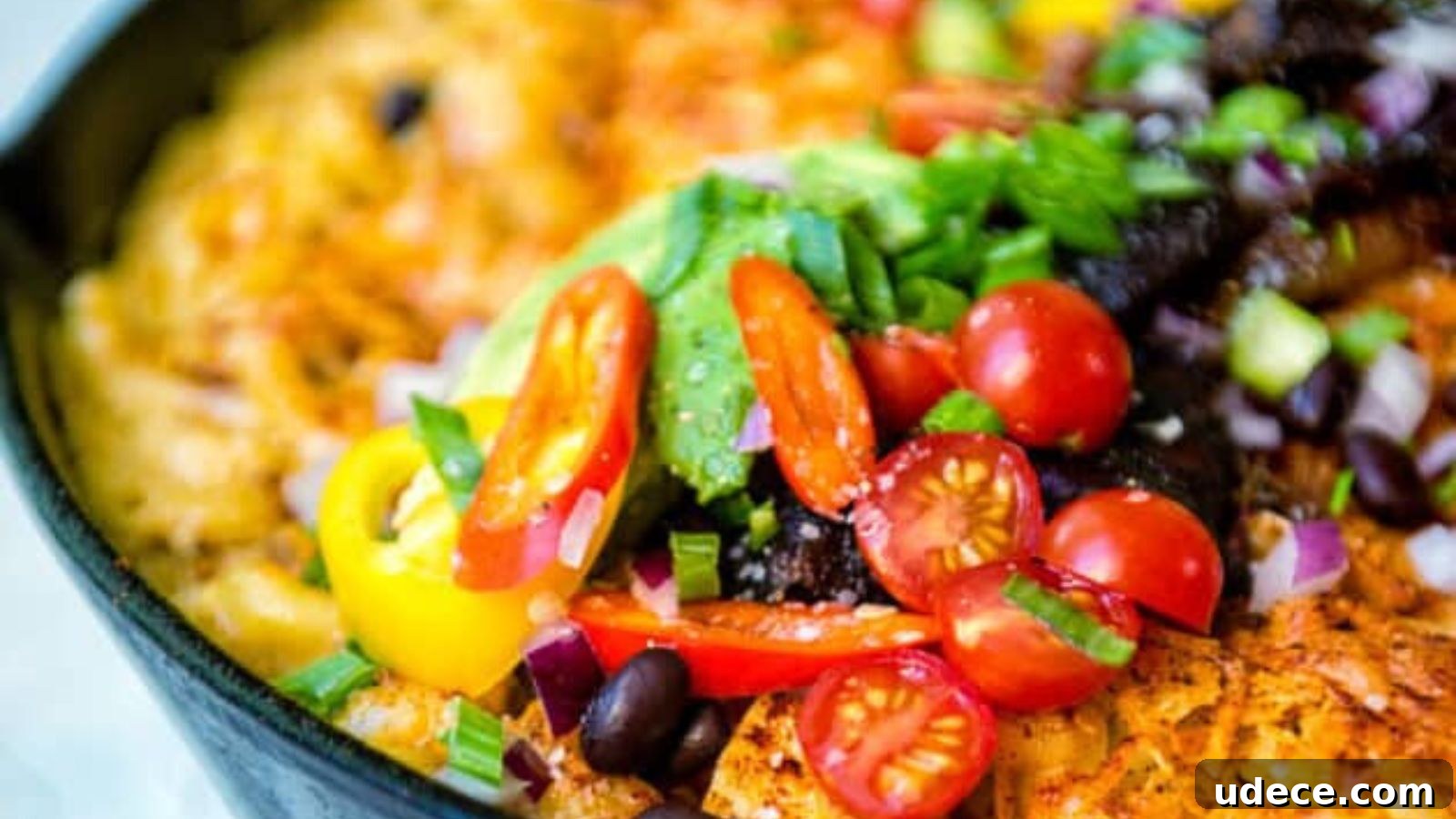 A colorful dish with cherry tomatoes, avocado, black beans, red onion, bell peppers, and a base layer visible in a black skillet.
